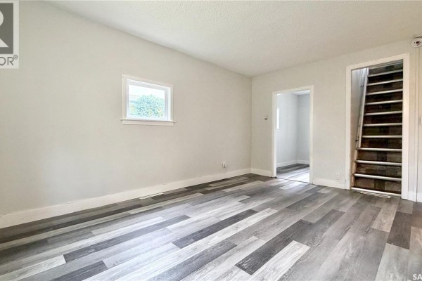 Living room showing an open doorway to another room and a staircase with dark treads. - 710 M Avenue S, Saskatoon