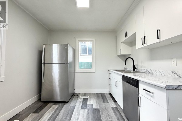 Kitchen with white cabinets, a stainless steel refrigerator, black faucet, and gray wood-look flooring. - 710 M Avenue S, Saskatoon
