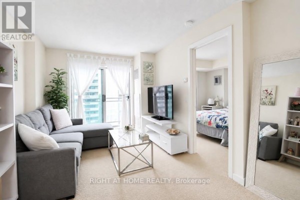 Living room with grey sectional sofa, glass coffee table, and television on stand. - 711 - 138 Somerset Street W, Ottawa