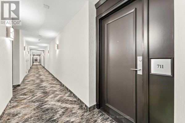 Interior view of a long apartment building hallway with patterned carpet and wall sconces. - 711 - 1403 Royal York Road, Toronto