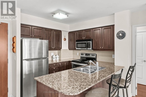Apartment kitchen with dark wood cabinets, stainless steel appliances, and granite countertops. - 711 - 1403 Royal York Road, Toronto