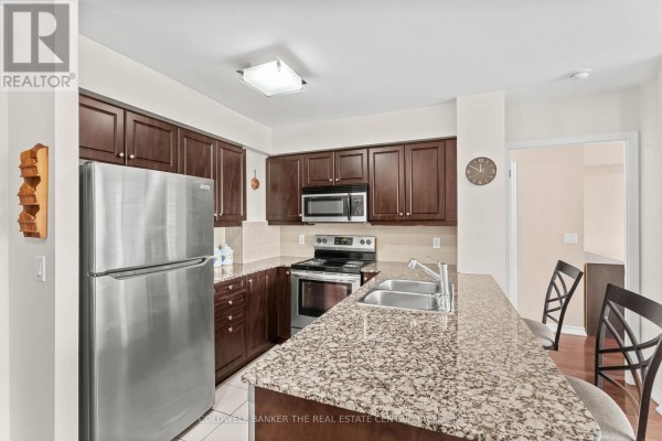 Apartment kitchen with dark wood cabinets, stainless steel appliances, granite countertops, and breakfast bar. - 711 - 1403 Royal York Road, Toronto