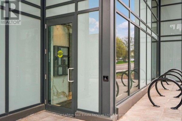 Close-up of a glass building entrance with a silver door and bike racks outside. - 711 - 2088 James Street, Burlington