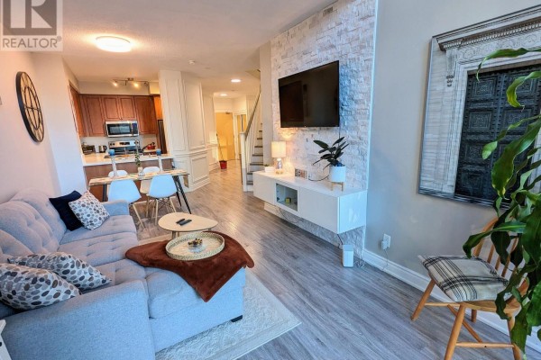 Living room featuring a grey sectional sofa, white entertainment unit, and stone accent wall. - 711 - 220 Burnhamthorpe Road W, Mississauga