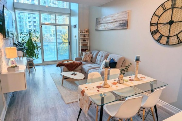 Living and dining area with a glass table, white chairs, and a large window. - 711 - 220 Burnhamthorpe Road W, Mississauga