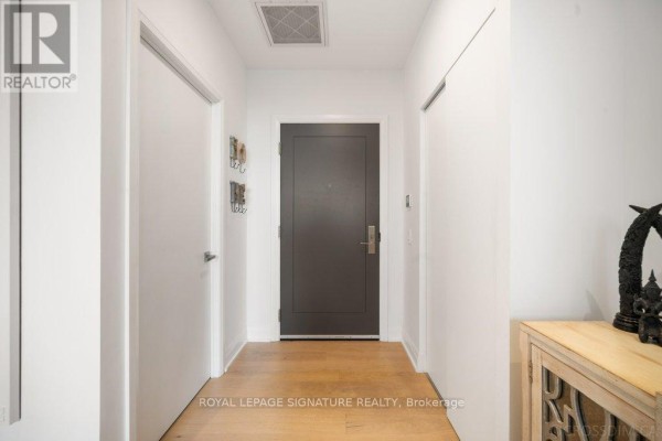 Apartment hallway with white walls, a dark grey door, light wood floor, and wooden cabinet. - 711 - 33 Frederick Todd Way, Toronto
