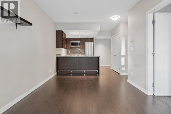 View of an open-concept living area with dark hardwood floors, leading to a kitchen with dark cabinets. - 711 1708 Columbia Street, Vancouver