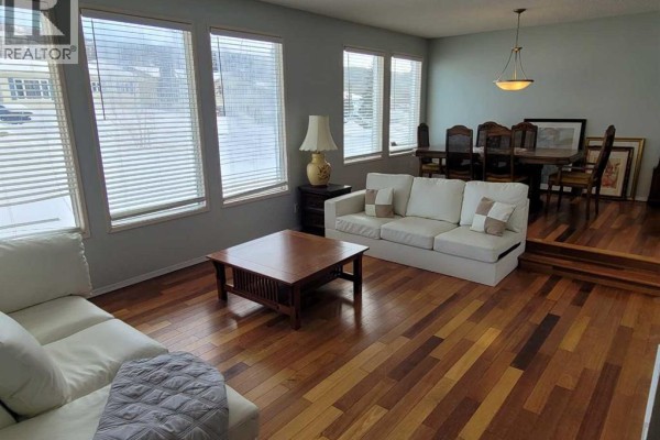 Living room featuring a dining area, large windows, and hardwood flooring - 7110 99a Street, Peace River