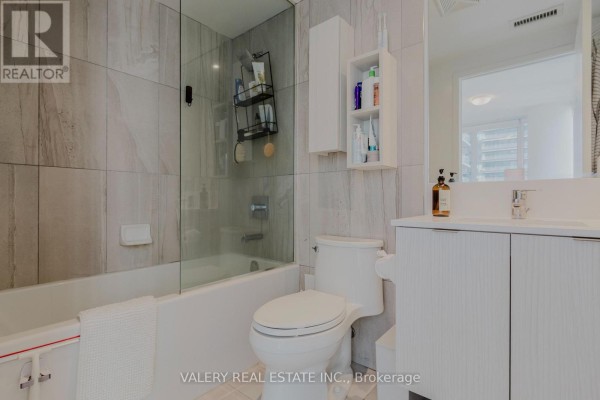 Bathroom with a bathtub, glass shower door, toilet, and white vanity with a sink and mirror. - 712 - 195 Redpath Avenue, Toronto