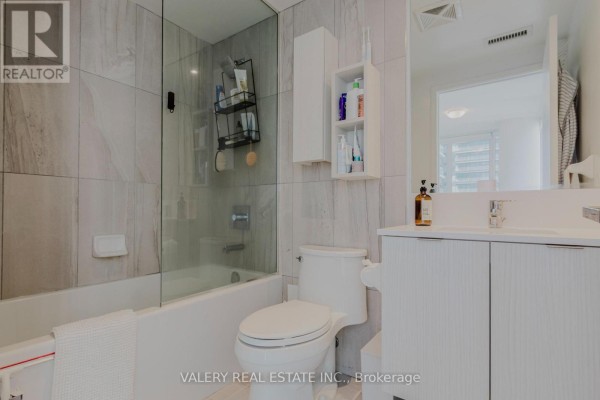 Bathroom with a bathtub, toilet, and white vanity. Tiled walls and a mirrored cabinet are visible. - 712 - 195 Redpath Avenue, Toronto