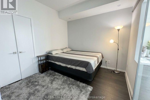 Bedroom with queen-size bed, nightstand, plush rug, and floor lamp. - 712 - 70 Temperance Street, Toronto