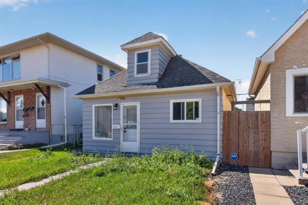 Side exterior view of a light blue siding house with a grey roof and a dormer. - 712 Martin Avenue E, Winnipeg