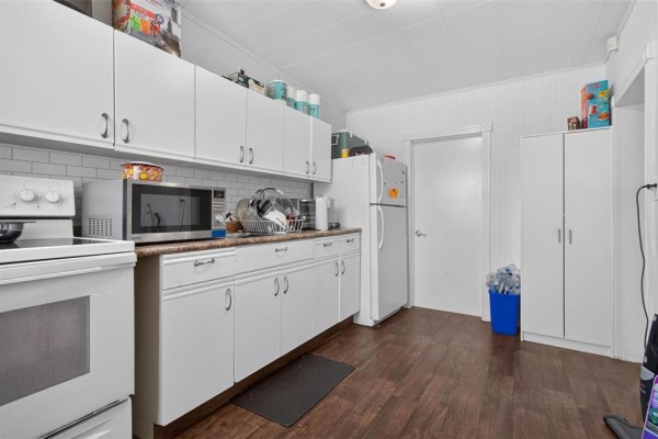 Kitchen showing white cabinets, white refrigerator, white stove, and dark wood-look floor. - 712 Martin Avenue E, Winnipeg