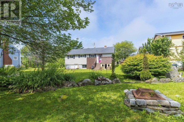 Backyard with green grass, large rocks, a stone fire pit, and mature trees. - 712 Old Sambro Road, Halifax