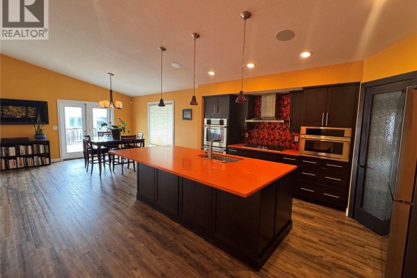Open-concept kitchen and dining area with a large orange island and dark cabinets. - 7122 Maple Vista Drive, Regina