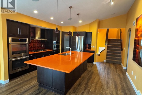 Kitchen island with stainless steel appliances, dark cabinetry, and orange countertops. Stairs are visible. - 7122 Maple Vista Drive, Regina