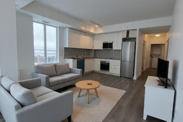 Living room and kitchen area with grey sofas, light wood coffee table, and white cabinets. - 713 - 2489 Taunton Road, Oakville