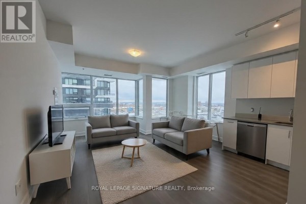 Living area with grey sofas, rug, and television facing large windows with city views. - 713 - 2489 Taunton Road, Oakville