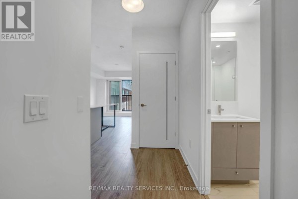 Interior hallway with light wood flooring, white doors, and a view into a living area and bathroom. - 713 - 30 Dreamer Way, Toronto