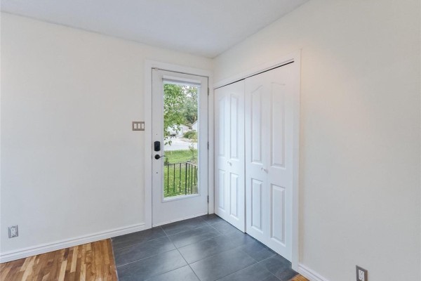 Interior entryway with dark grey tile floor, white bi-fold closet doors, and a glass-paneled door to the outside. - 713 Buckingham Road, Winnipeg