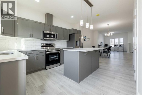 Modern kitchen with gray cabinets, stainless steel appliances, and an island - 713 Clearview Green, Chestermere