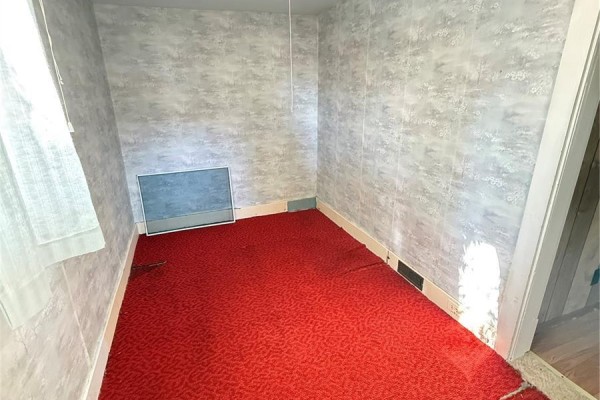 Bedroom with red carpet, patterned wallpaper, and a window with sheer curtains. - 713 Healy Avenue, Radville
