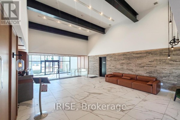 Spacious apartment building lobby with white marble tile floors, exposed beams, and a brown leather sofa. - 714 - 2300 St. Clair Avenue W, Toronto