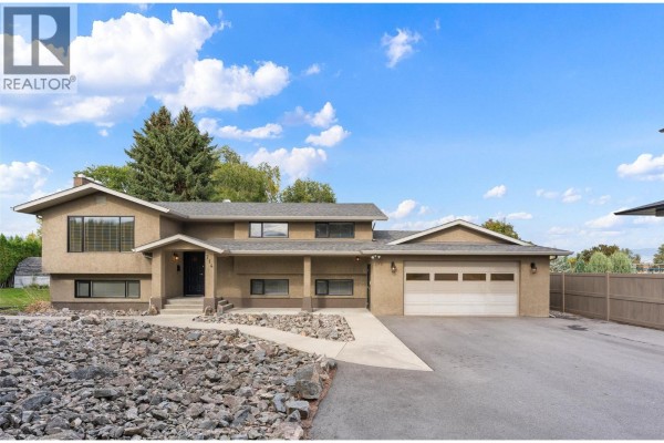 Front exterior of a residential home with a paved driveway and mature trees under a blue sky. - 714 Turner Road, Kelowna