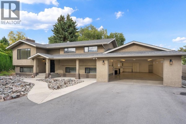Side view of the house showing the open garage doors and paved driveway. - 714 Turner Road, Kelowna