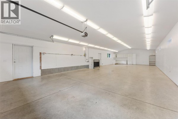 Interior of a large, empty garage with concrete floors, white walls, and rows of fluorescent lighting. - 714 Turner Road, Kelowna