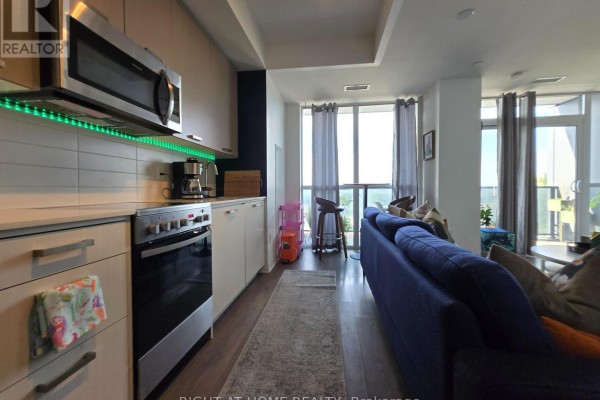 Kitchenette with stainless steel appliances, beige cabinets, and green under-cabinet lighting. - 715 - 2301 Danforth Avenue, Toronto
