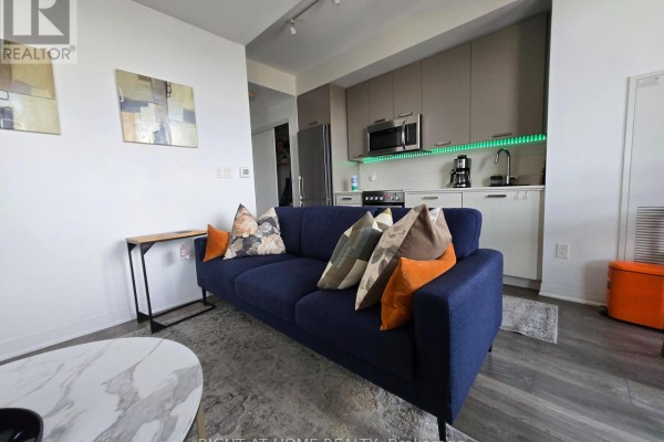 Open concept living space with a navy sofa, coffee table, and view of the kitchenette. - 715 - 2301 Danforth Avenue, Toronto