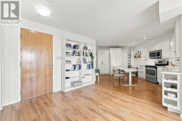 Open concept living and dining area with hardwood floors, white shelves, and a modern kitchen. - 715 - 340 Watson Street W, Whitby