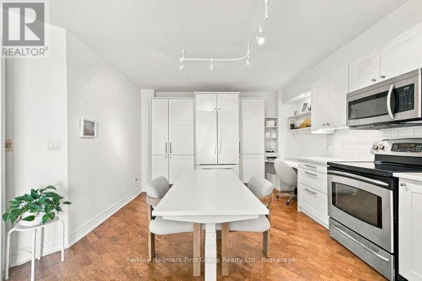 Dining area in front of white cabinets and a modern kitchen with stainless steel appliances. - 715 - 340 Watson Street W, Whitby