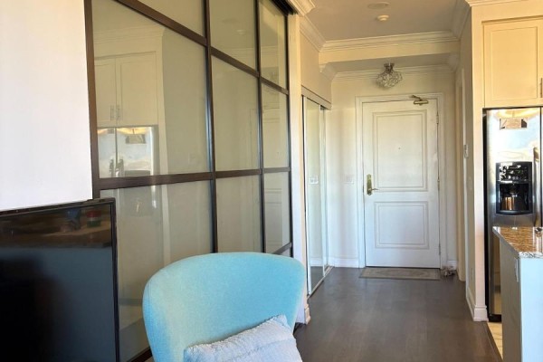 Interior view showing a blue armchair, glass-paneled closet doors, and a kitchen with stainless steel appliances. - 715 - 9245 Jane Street, Vaughan