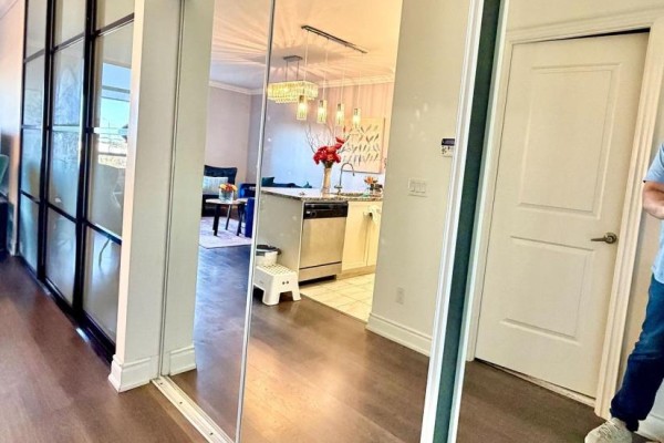 Reflection in mirrored closet doors shows a living area with a sofa, chairs, kitchen island, and chandelier. - 715 - 9245 Jane Street, Vaughan
