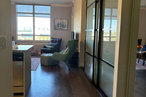 Living area with two armchairs, a coffee table, and large windows with a city view beyond. Dark wood floor. - 715 - 9245 Jane Street, Vaughan