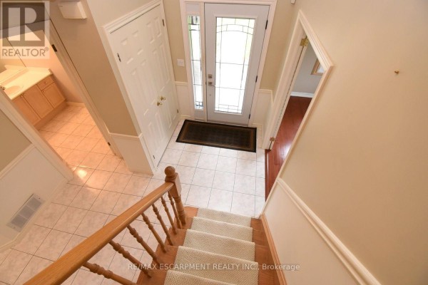 Interior foyer with a light carpeted staircase, wood railings, and ceramic tile flooring. - 715 Bateman Court, Burlington