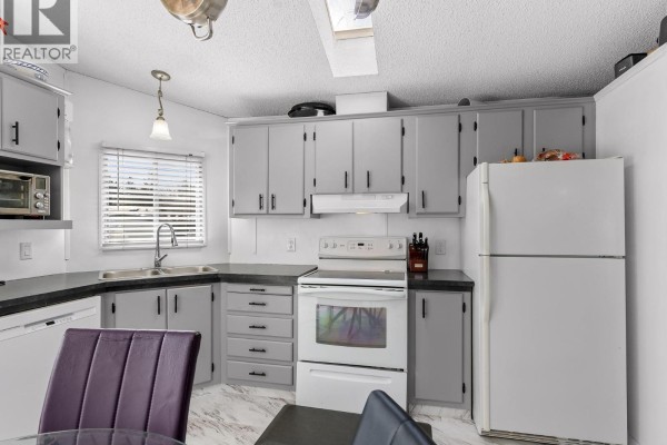 Kitchen and dining area with white cabinets, black countertops, and a glass table with chairs. - 715 Beaver Lake Road Unit# 94, Kelowna