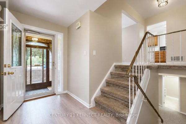 Foyer with beige walls, light wood laminate flooring, carpeted stairs with a metal railing, and glass-paneled front doors. - 715 Waverly Street N, Oshawa