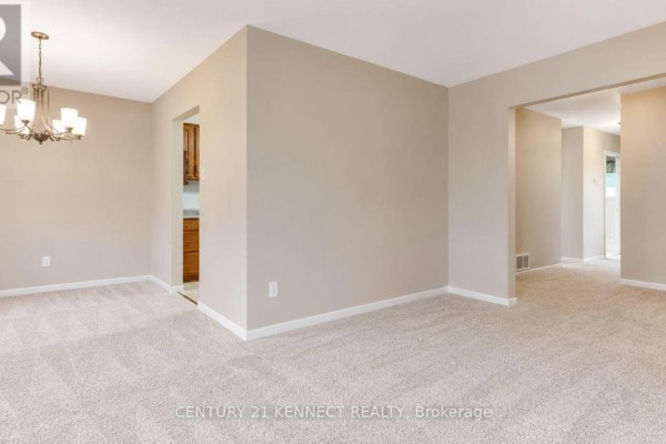 View of the beige carpeted dining and living area, showing an archway leading to a hallway. - 715 Waverly Street N, Oshawa