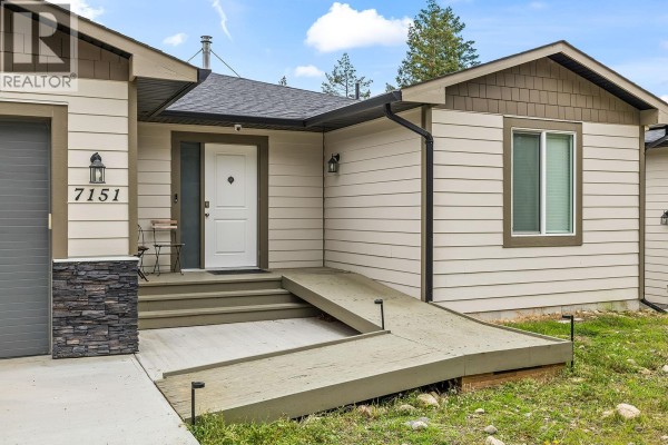 Close-up of the front entrance of a beige house with a white door, accessible ramp, and stone accent. - 7151 Dunwaters Road, Kelowna
