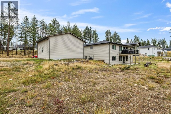 Rear exterior view of the house and detached garage on a grassy lot with pine trees. - 7151 Dunwaters Road, Kelowna