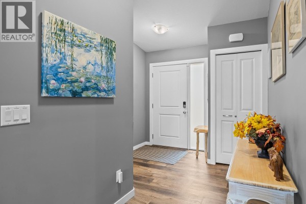 Interior hallway with grey walls, wood-look flooring, double white doors, and decorative artwork. - 7151 Dunwaters Road, Kelowna