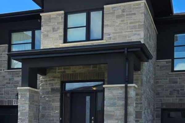 Front facade of a modern townhouse with stone and black siding, featuring a covered entryway. - 7157 Parsa Street, Niagara Falls