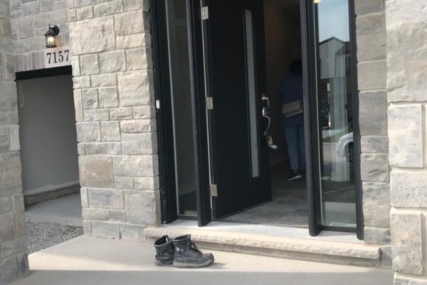 Open front doors of a townhouse with stone exterior, showing a glimpse of the interior hallway. - 7157 Parsa Street, Niagara Falls