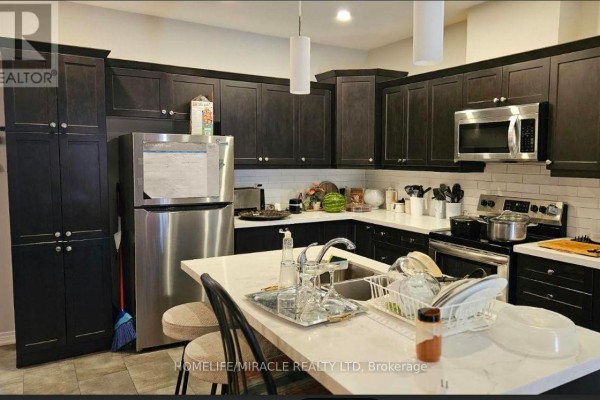 Kitchen with dark wood cabinets, stainless steel refrigerator, black countertops, and white tiled backsplash. - 7157 Parsa Street, Niagara Falls