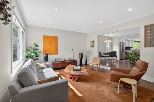 Living room with a view into the dining area and kitchen, featuring a grey sofa and orange rug. - 7159 York Crescent, Delta