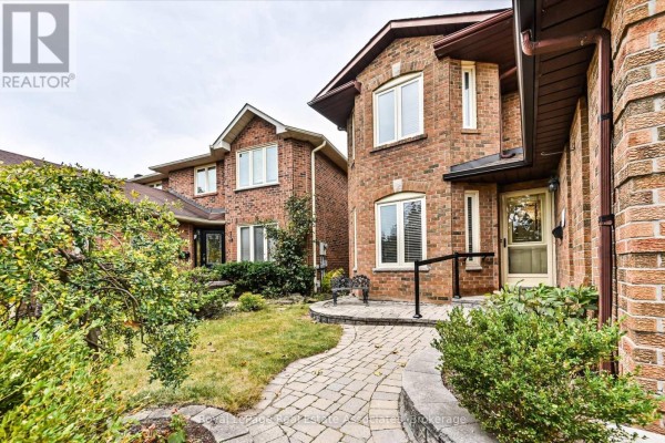 Walkway leading to the front entrance of the house with green bushes and trees. - 7164 Danton Promenade, Mississauga