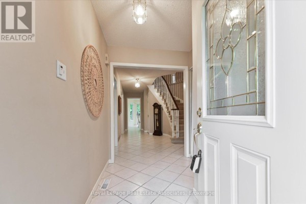 Interior view of a bright entryway with tiled floors, a staircase, and a grandfather clock. - 7164 Danton Promenade, Mississauga